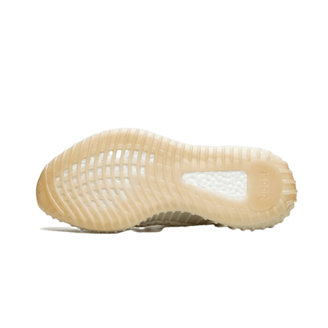 Crèmewitte Adidas Yeezy Boost 350 V2 Light sneakers met opvallende textuur en perforaties op de zool, geplaatst op een effen groene achtergrond.