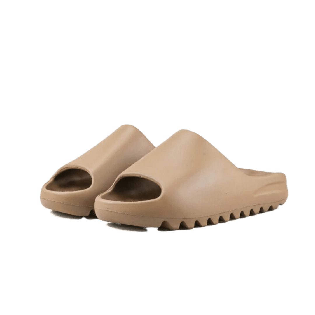 Beige Adidas Yeezy Slide sandalen in aardbruin op groen oppervlak