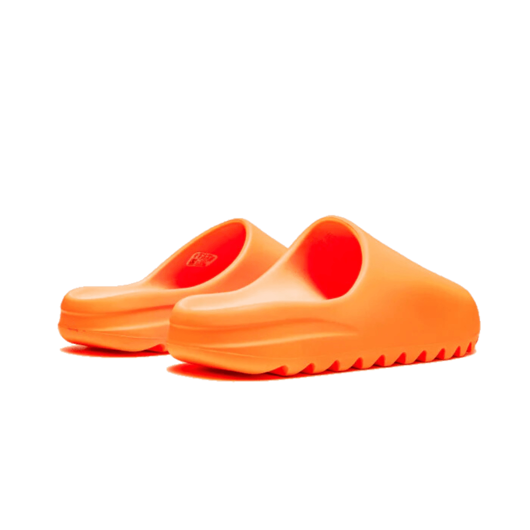 Opvallende Adidas Yeezy Slide Enflame Orange slippers tegen groene achtergrond