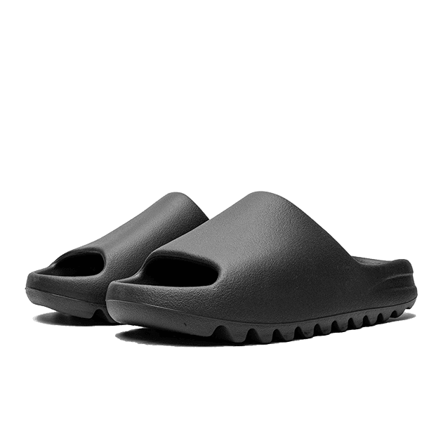 Zwarte Adidas Yeezy Slide Onyx sandalen op een effen groene achtergrond. De sandalen hebben een karakteristiek design met een comfortabele, massieve zool.
