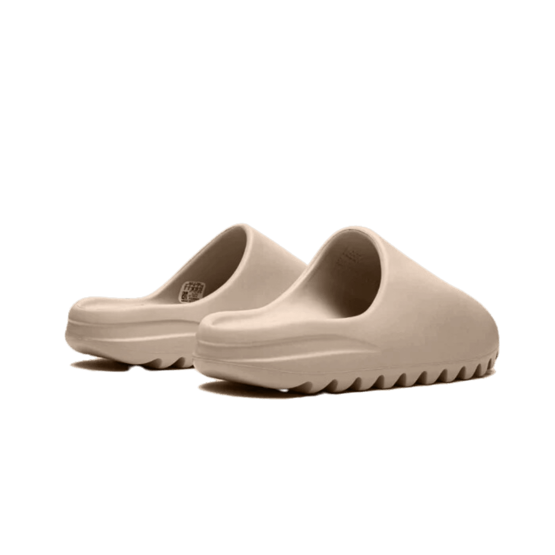 Getoonde Adidas Yeezy Slide Pure (First Release) slippers in beige kleur op groene achtergrond. De slippers hebben een uniek ontwerp met dikke zolen voor een comfortabele pasvorm.