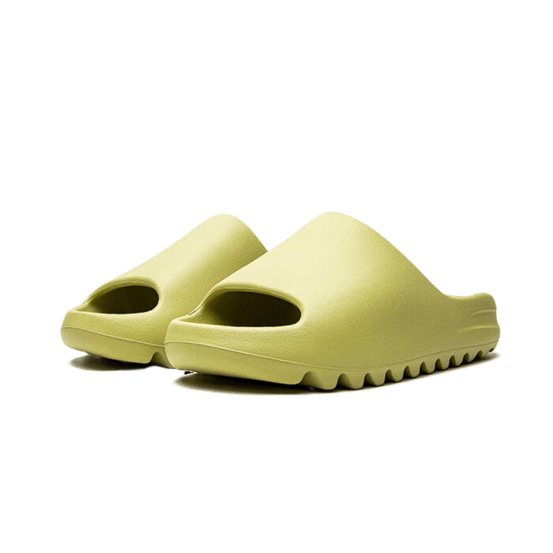 Gele Adidas Yeezy Slide Resin (Restock Pair) slippers op een groene achtergrond.