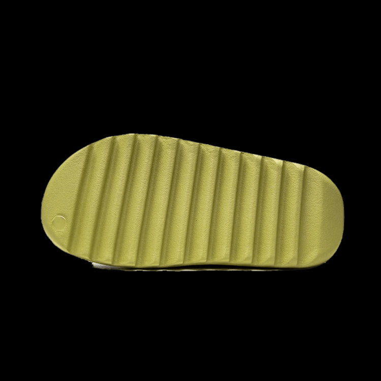 Goudkleurige Adidas Yeezy Slide Resin (Restock Pair) slippers op groene achtergrond.