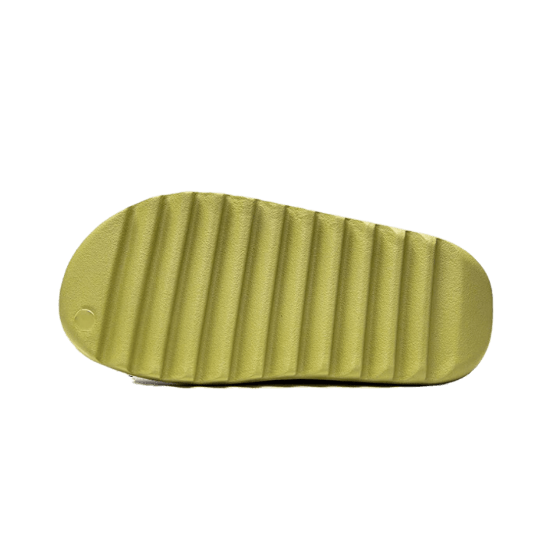 Goudkleurige Adidas Yeezy Slide Resin (Restock Pair) slippers op groene achtergrond.