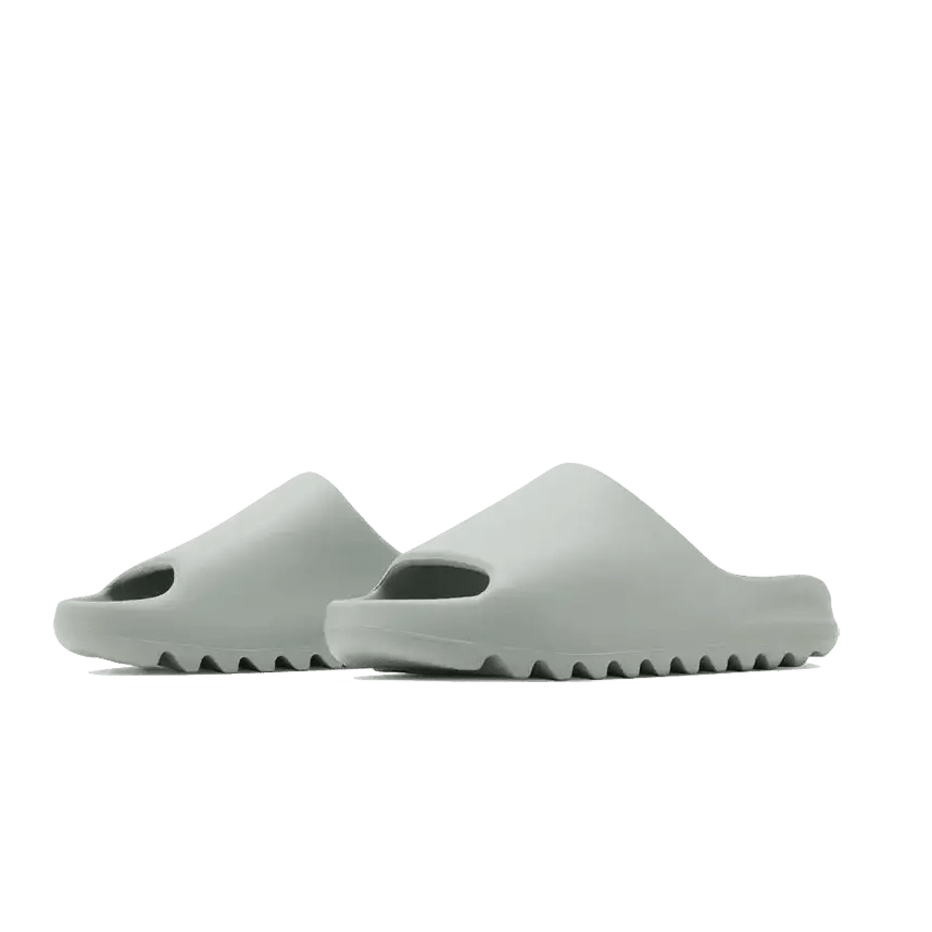 Adidas Yeezy Slide Salt, moderne lichtgrijze sandalen met duidelijk profiel op de groene achtergrond.