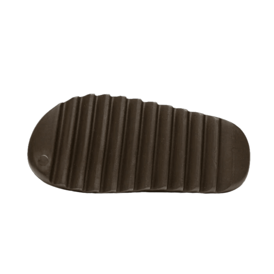 Dikke, geribbelde zool van zwarte Adidas Yeezy Slide Soot sneakers, geplaatst op een groene achtergrond.