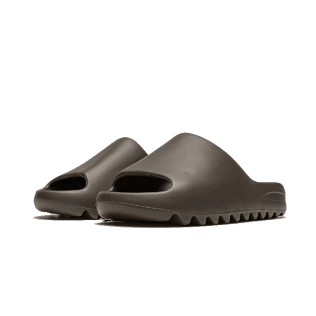 Grijze Adidas Yeezy Slide Soot sandalen op effen groene achtergrond. Deze comfortabele en stijlvolle slippers zijn geschikt voor alledaags gebruik.