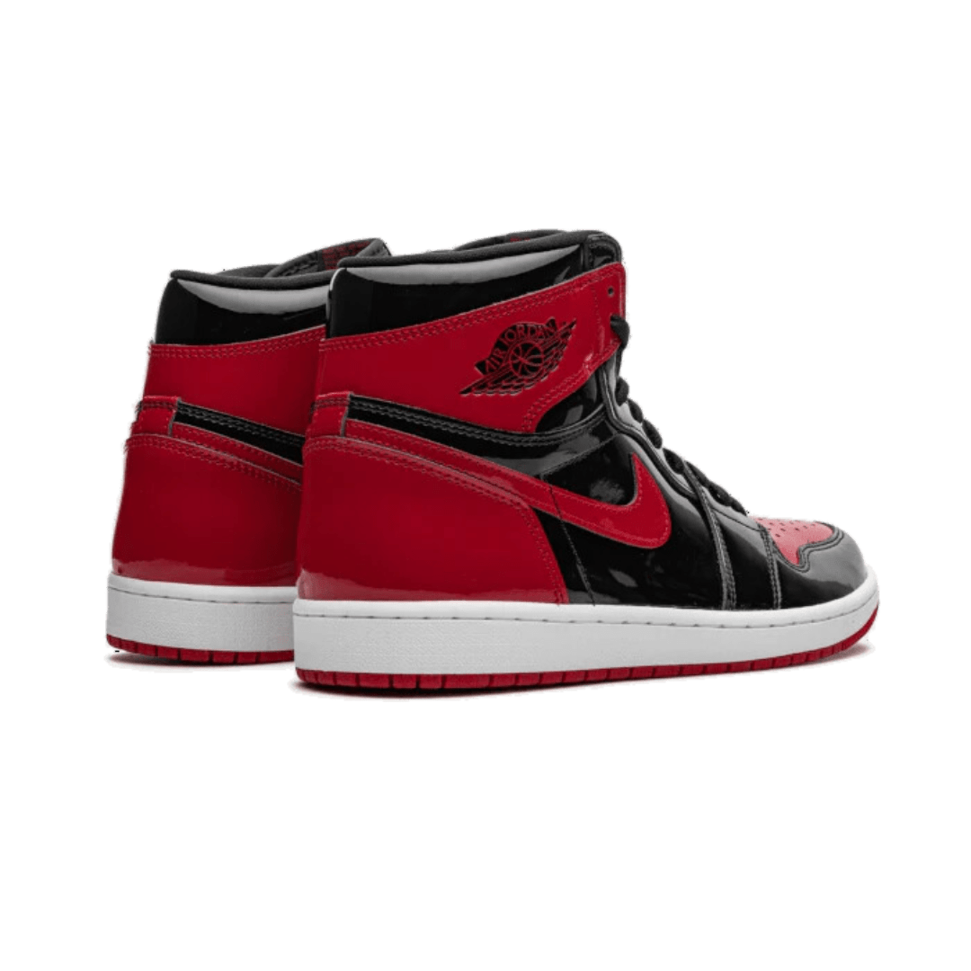 Rode en zwarte Air Jordan 1 High OG Patent Bred sneakers op groene achtergrond. Exclusieve en iconische basketbal-schoen met kenmerkende Nike-swoosh en Air Jordan-logo.