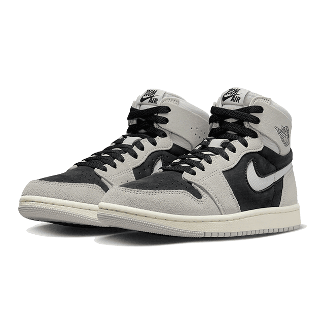 Stoere, licht-grijze Nike Air Jordan 1 High Zoom Air CMFT 2-sneakers met zwart detail op een groene achtergrond.