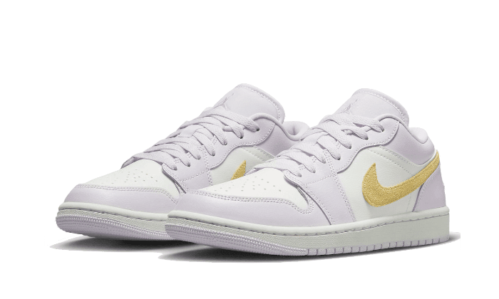 Witte en gouden Nike Air Jordan 1 Low Barely Grape sneakers op een groen oppervlak. De schoenen hebben een modieus en elegant uiterlijk met hun kleurpatroon en opvallende swoosh-logo.