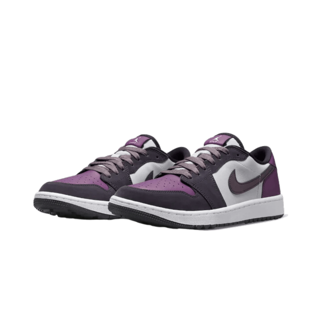 Een paar Nike Air Jordan 1 Low Golf NRG Purple Smoke sneakers op een groene achtergrond. De sneakers hebben een paars en grijs kleurenontwerp met de herkenbare Nike swoosh logo. Het zijn stijlvolle en hoogwaardige golfschoenen die je look op de baan compleet maken.