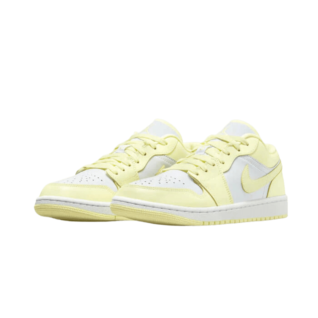 Gele Nike Air Jordan 1 Low Lemonade sneakers op een groene achtergrond. Deze schoenen hebben een lichtgele suède bovenwerk met witte leren accenten en een witte rubberen zool. De sneakers hebben een stijlvolle en elegante uitstraling en zijn geschikt voor dagelijks gebruik.