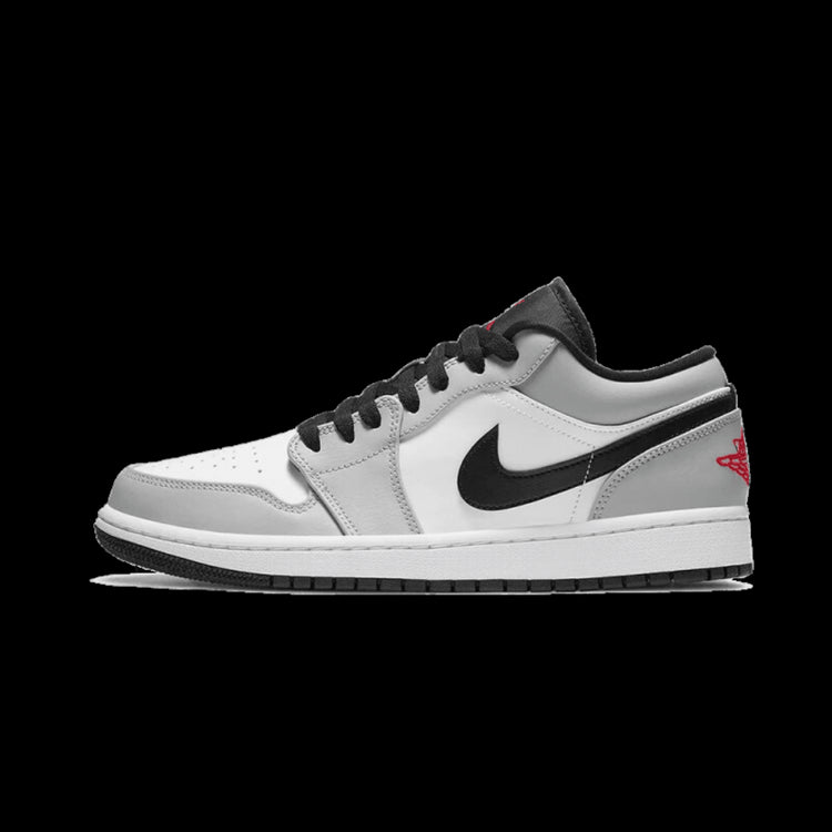 Grijze Air Jordan 1 Low Light Smoke sneakers tegen een groene achtergrond. De sneakers hebben een wit en zwart design met de kenmerkende Nike-logo op de zijkant.