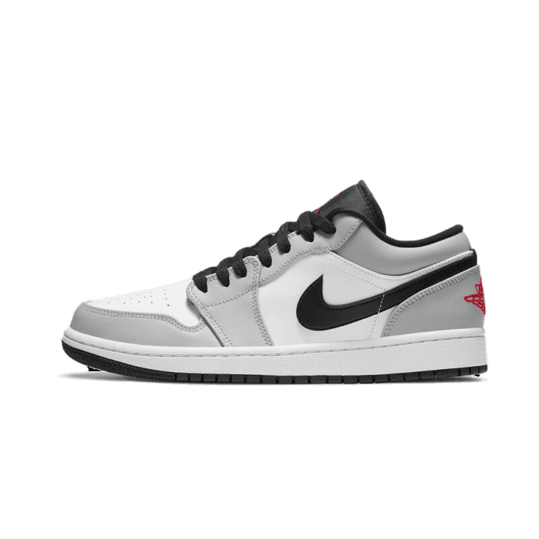 Grijze Air Jordan 1 Low Light Smoke sneakers tegen een groene achtergrond. De sneakers hebben een wit en zwart design met de kenmerkende Nike-logo op de zijkant.