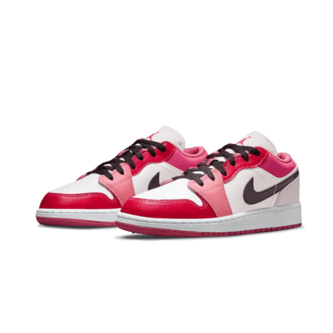 Een paar roze Nike Air Jordan 1 Low sneakers op een groene achtergrond. De sneakers hebben een wit, rood en zwart kleurpatroon en zien er modern en sportief uit.