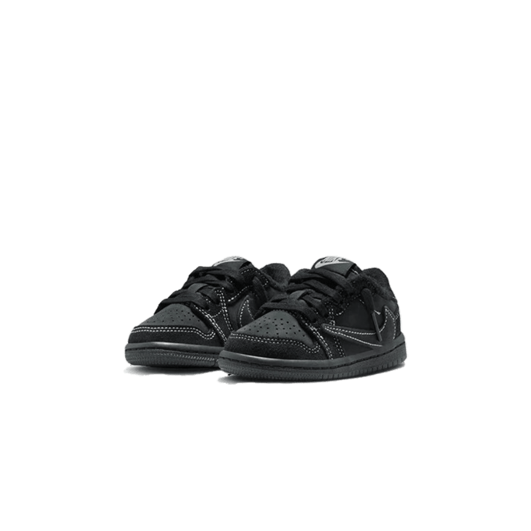 Kleine zwarte en grijze Nike Air Jordan 1 Low SP Travis Scott Phantom Bébé (TD) sneakers op een groene achtergrond. De schoenen hebben een klassiek ontwerp en zijn ideaal voor de jongste sneakerfanaten.