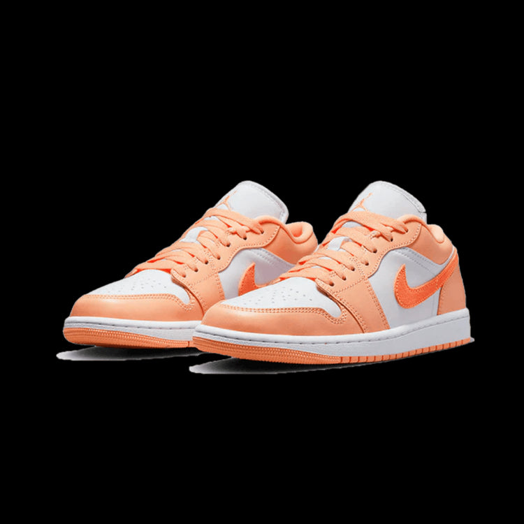 Een paar Nike Air Jordan 1 Low Sunset Haze sneakers, geplaatst op een effen groene achtergrond. De sneakers hebben een oranje suède en witte lederen bovenzijde, met het kenmerkende Nike Swoosh-logo op de zijkant. De zool heeft een oranje en witte ombré-effect.