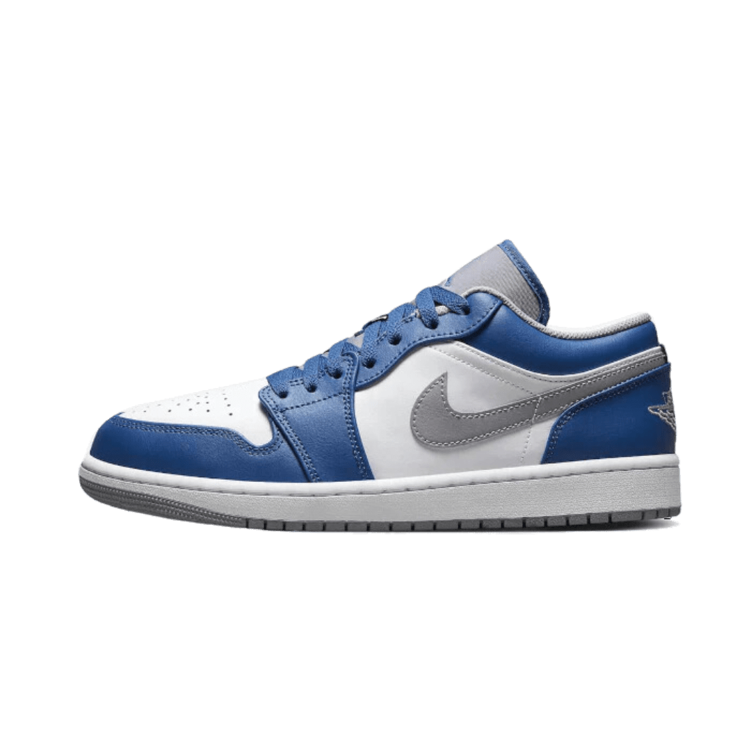 Blauwe en witte Nike Air Jordan 1 Low True Blue sneakers op een groen oppervlak. De sneakers hebben een klassiek design met een leren bovenkant, zichtbare Nike-swoosh, en een rubberen zool voor goede grip.