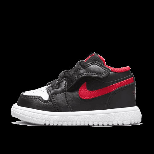 Lage sneakers Air Jordan 1 Low White Toe Bébé (TD) voor kleine kinderen in zwart-wit en rood ontwerp van het merk Nike. Getoond op een groene achtergrond.
