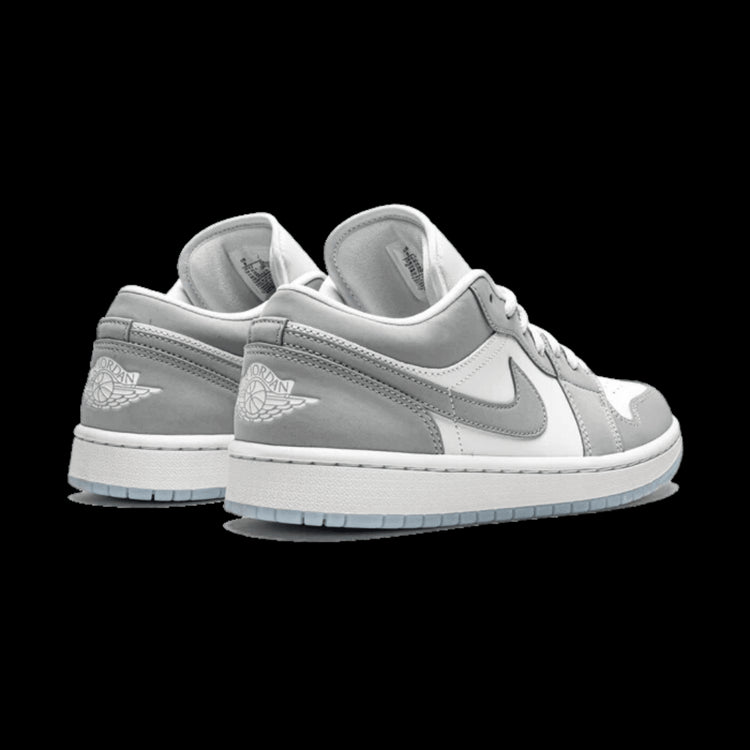 Grijze Nike Air Jordan 1 Low sneakers met grijs lederen voorkant en zool tegen effen groene achtergrond.
