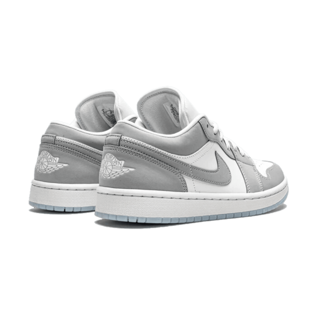 Grijze Nike Air Jordan 1 Low sneakers met grijs lederen voorkant en zool tegen effen groene achtergrond.