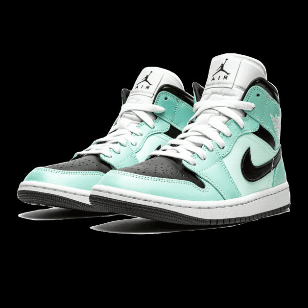 Pastelkleurige Air Jordan 1 Mid Aqua Blue Tint sneakers op een groene achtergrond getoond. De sneakers hebben een combinatie van wit, zwart en een lichtblauwe tint, met Nike Air-branding op de zijkant.