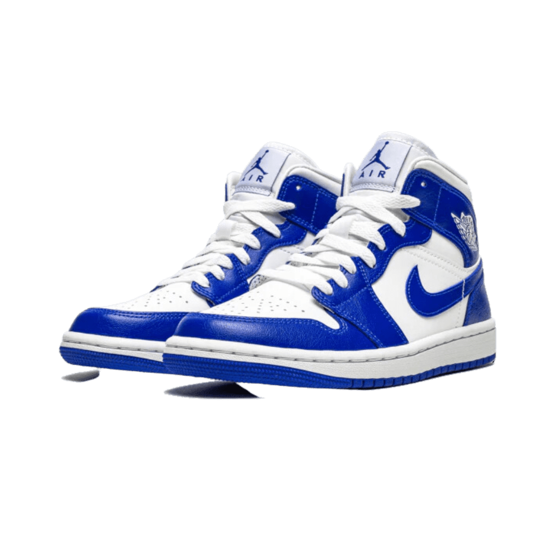 Paar blauwe en witte Nike Air Jordan 1 Mid Kentucky sneakers weergegeven op een groene achtergrond. De sneakers kenmerken het karakteristieke ontwerp van de Air Jordan 1 met het iconische Nike swoosh-logo.