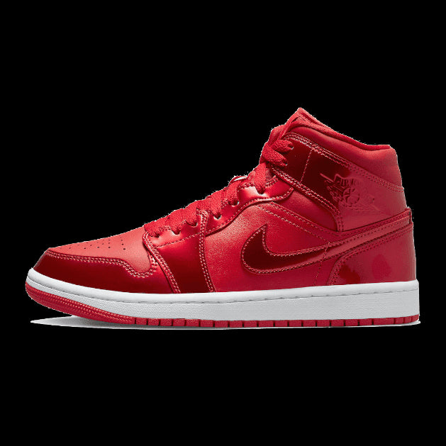 Rode Nike Air Jordan 1 Mid SE Pomegranate sneakers tegen een groene achtergrond. Deze trendy sneakers hebben een rood suède bovenstuk met kenmerkende Nike Swoosh en Air Jordan logo's.