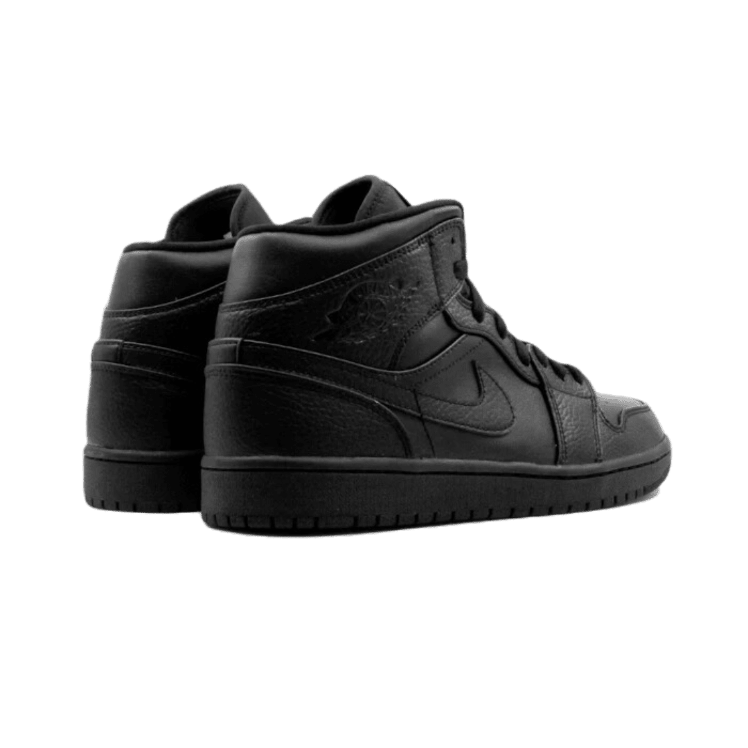 Zwarte Air Jordan 1 Mid sneakers op een effen groene achtergrond