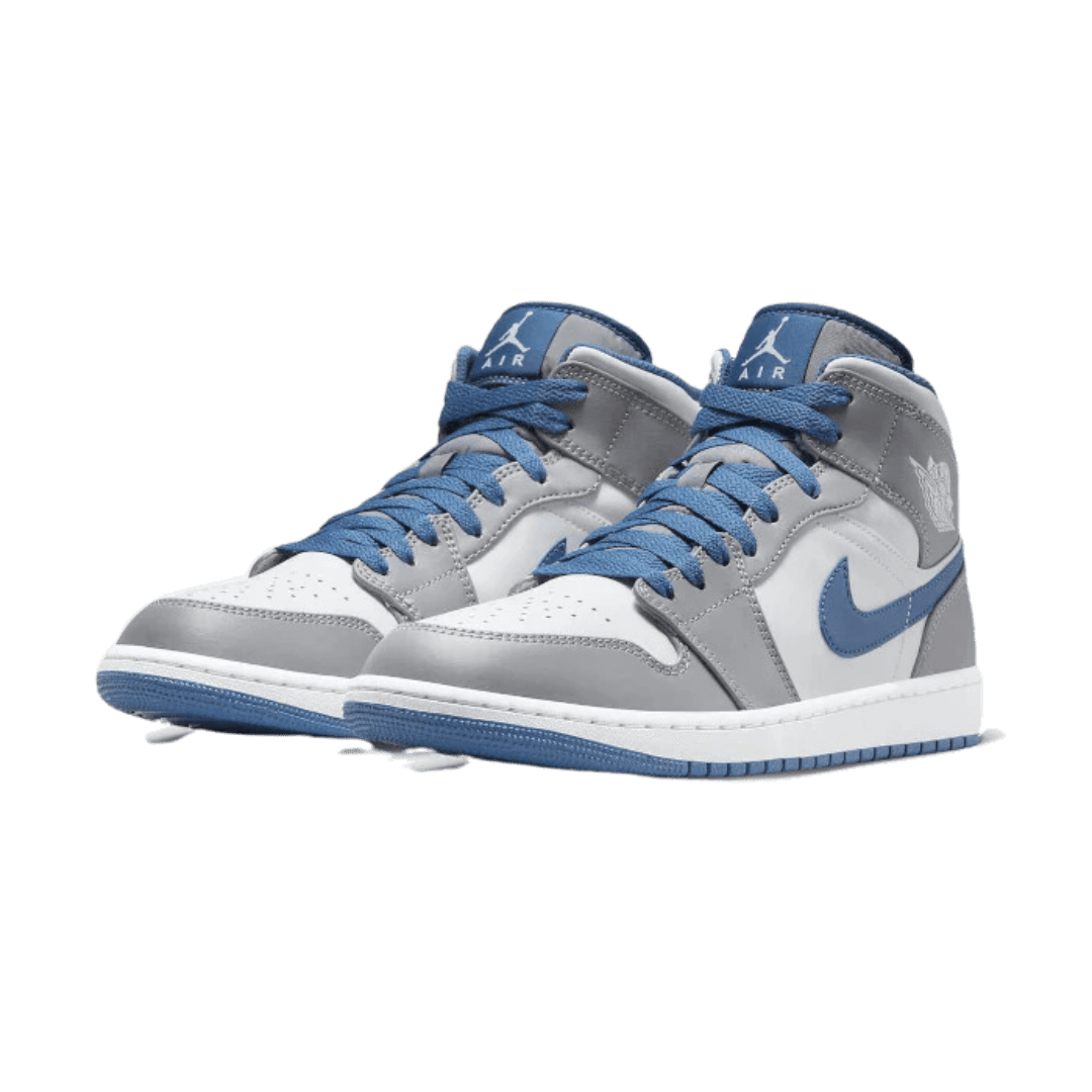 Stijlvolle Air Jordan 1 Mid True Blue sneakers op groene achtergrond. Deze klassieke basketbalschoenen van Nike hebben een opvallende grijze bovenste, blauwe accenten en een comfortabele pasvorm.