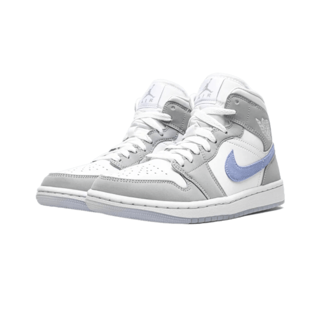 Witte, grijze en blauwe Nike Air Jordan 1 Mid sneakers met een klassiek ontwerp op een groene achtergrond.