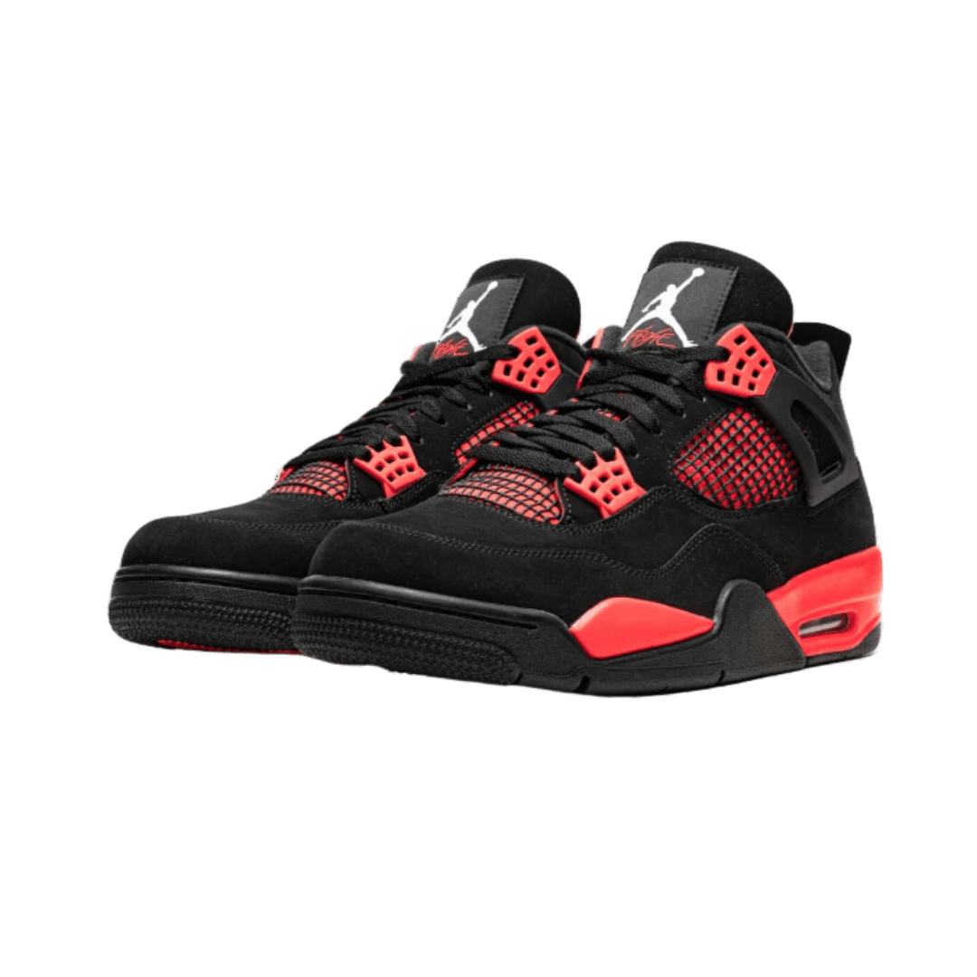 Zwarte Air Jordan 4 Retro sneakers met rode accenten en een geperforeerd patroon op het oppervlak, tegen een groene achtergrond geplaatst.