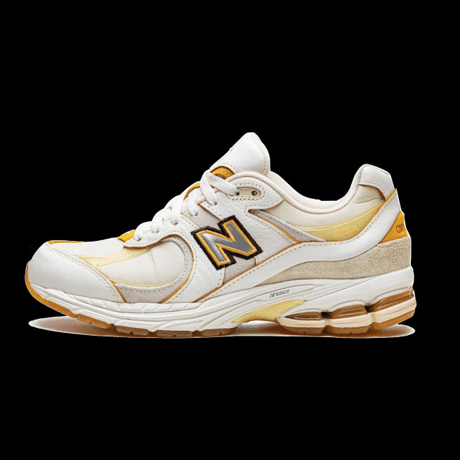 Nieuwe Balance 2002R sneakers in wit en goud, met het karakteristieke New Balance-logo. Deze sneakers laten een sportieve en stijlvolle uitstraling zien.