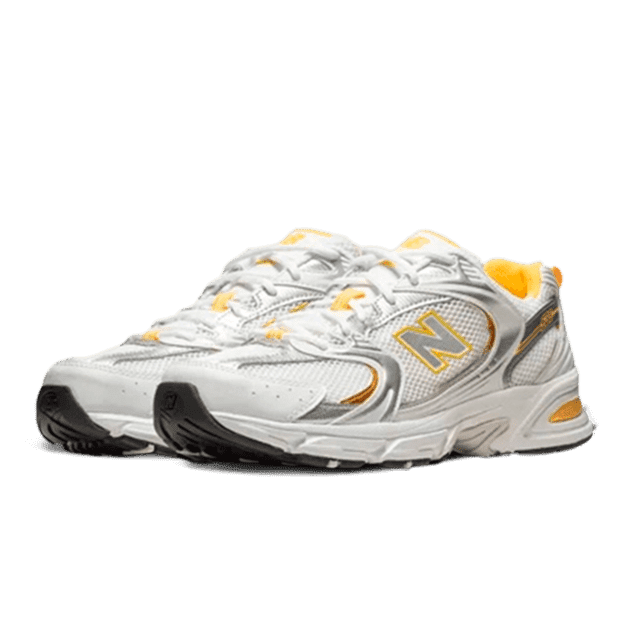Moderne New Balance 530 sneakers in een wit, zilver en gele kleurstelling. De schoenen hebben een rubberen zool voor stabiliteit en grip, en de geperforeerde bovenlaag biedt ventilatie. Een stijlvol en comfortabel paar sportschoenen.