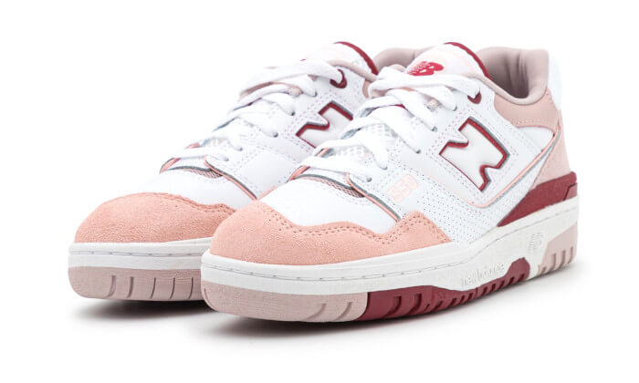 Nieuwe Balance 550 sneakers in wit, scarlet roze en rood. De sneakers hebben een stijlvolle mix van materialen zoals leer en mesh, en een opvallende N-logo op de zijkant. Deze sneakers combineren klassieke details met moderne accenten, waardoor ze een tijdloze en trendy uitstraling hebben.