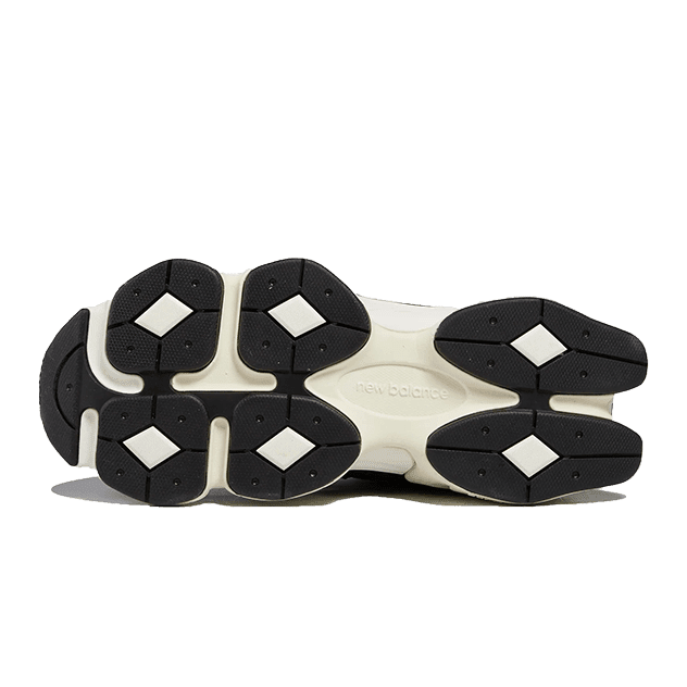 Zwarte en witte New Balance 9060 sneakers op een groene achtergrond. De zool heeft een opvallend, gedetailleerd ontwerp met geometrische vormen.