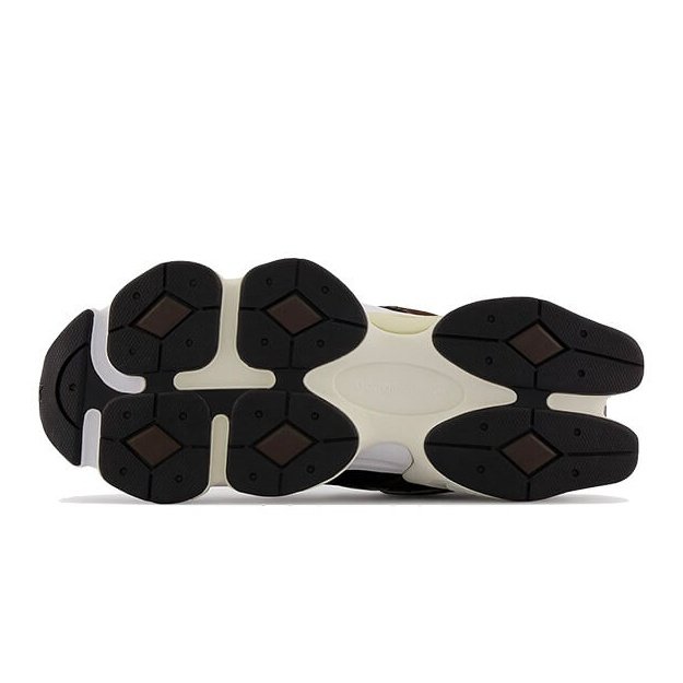 Donkergekleurde New Balance 9060 sneakers weergegeven op een witte achtergrond. De rubberen zool met duidelijke profielstructuur is zichtbaar, wat een sportieve look en grip suggereert.
