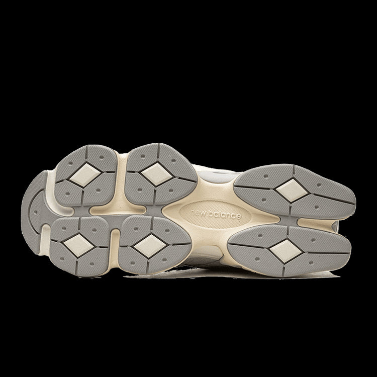 Nieuwe New Balance 9060 Quartz sneakers op een groene achtergrond. De sneakers hebben een grijze, witte en goudkleurige zool met diamantvormige details voor een unieke en stijlvolle uitstraling.