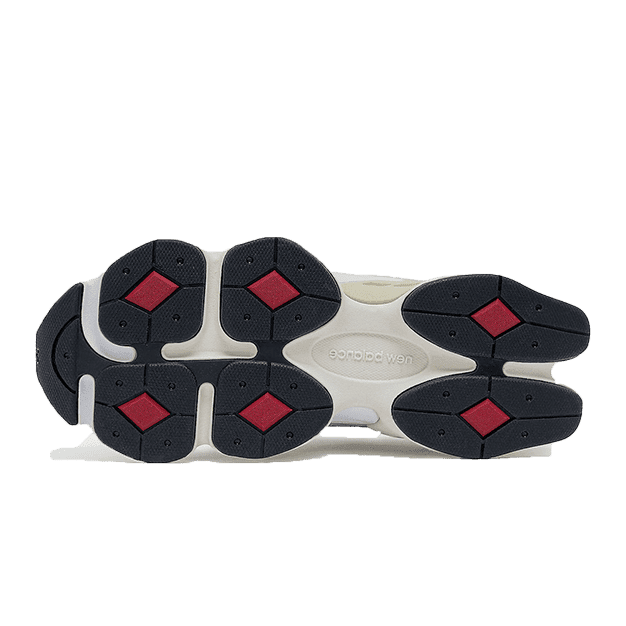 Witte en zwarte New Balance 9060 sneakers op een groene achtergrond. De sneakers hebben een moderne look met rode accenten op de zool. De schoenen zijn geschikt voor actief gebruik dankzij het dempende loopcomfort.