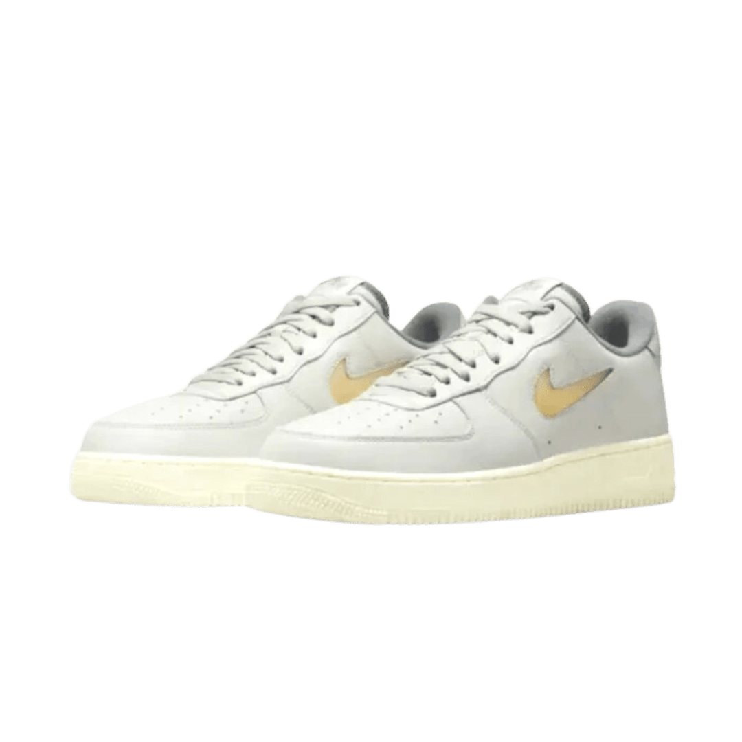 Elegant paar Nike Air Force 1 Low sneakers in lichte beige kleur met gouden accenten op een donkergroene achtergrond. De klassieke sneakers hebben een sportieve uitstraling en zijn een modetrend.