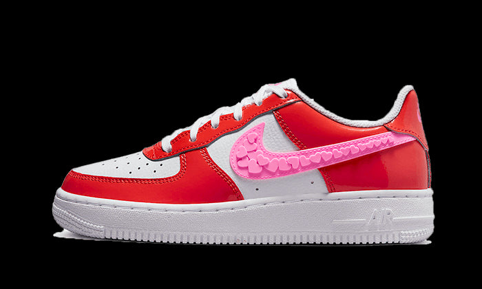 Rode Nike Air Force 1 Low Valentine's Day (2023) sneakers met witte details en een roze bloemenversieringen op een groene achtergrond.