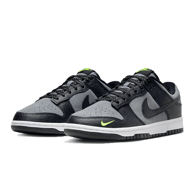 Zwarte en grijze Nike Dunk Low sneakers met groene accenten op een donkergroen oppervlak.