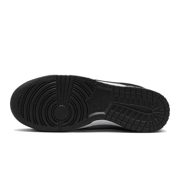 Zwart, grijs en oranje Nike Dunk Low sneakers met een robuuste, ribbelprofielzool op een effen groene achtergrond.