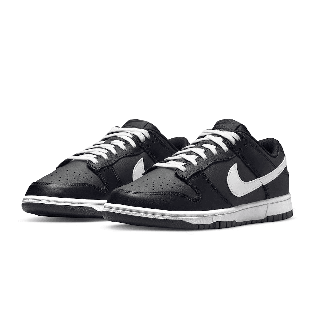 Zwarte en witte Nike Dunk Low sneakers in het midden van het beeld op een groene achtergrond. De sneakers hebben een stijlvol en minimalistisch ontwerp met het Nike logo prominent zichtbaar.