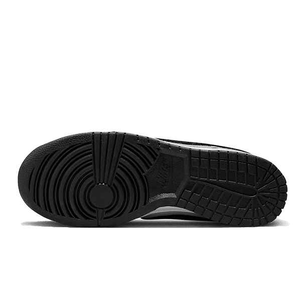 Zwarte Nike Dunk Low Chenille Swoosh sneaker met zwarte ribbelzool tegen een groene achtergrond.