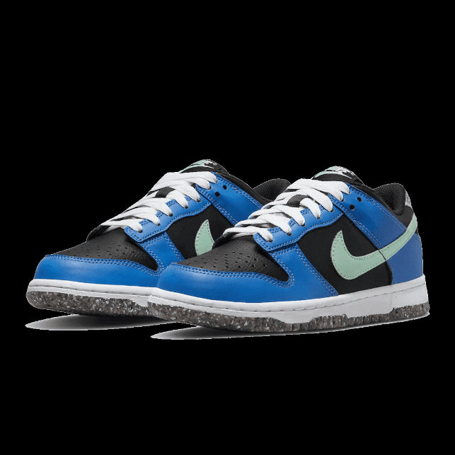 Blauwe en zwarte Nike Dunk Low Crater Light Photo sneakers op een groen oppervlak. Deze moderne sportieve schoenen hebben een opvallende kleurencombinatie, een geribbelde zool voor extra grip en een duurzaam ontwerp met gerecycled materiaal.