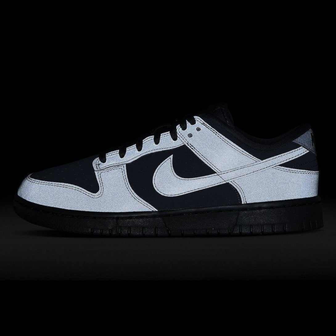 Zwart-witte Nike Dunk Low Cyber Reflective sneakers op een zwarte achtergrond. De schoen heeft een opvallend zwart-wit ontwerp met reflecterende details voor een dynamische look. Dit model is een populaire keuze onder sneakerliefhebbers die stijl en functionaliteit zoeken.