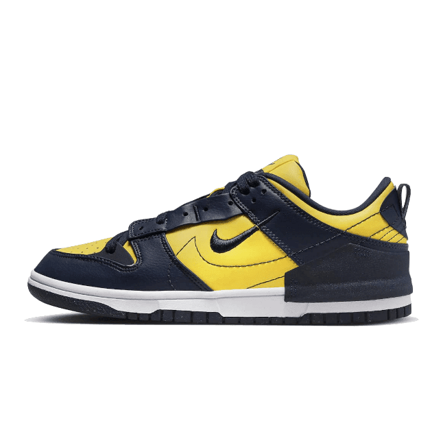 Gele en zwarte Nike Dunk Low Disrupt 2 Michigan sneakers op een groene achtergrond