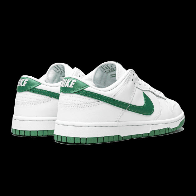 Witte Nike Dunk Low sneakers met groene details op een groen achtergrond. De klassieke sportstijl van Nike is prominent zichtbaar in het ontwerp. De sneakers zijn perfect geschikt voor casual en sportieve stijlen.
