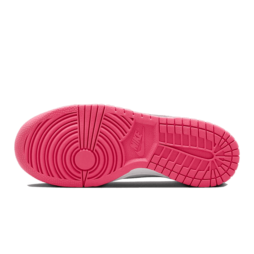 Roze Nike Dunk Low sneakers met een opvallend en geribbeld rubberen zoolpatroon op een groene achtergrond.